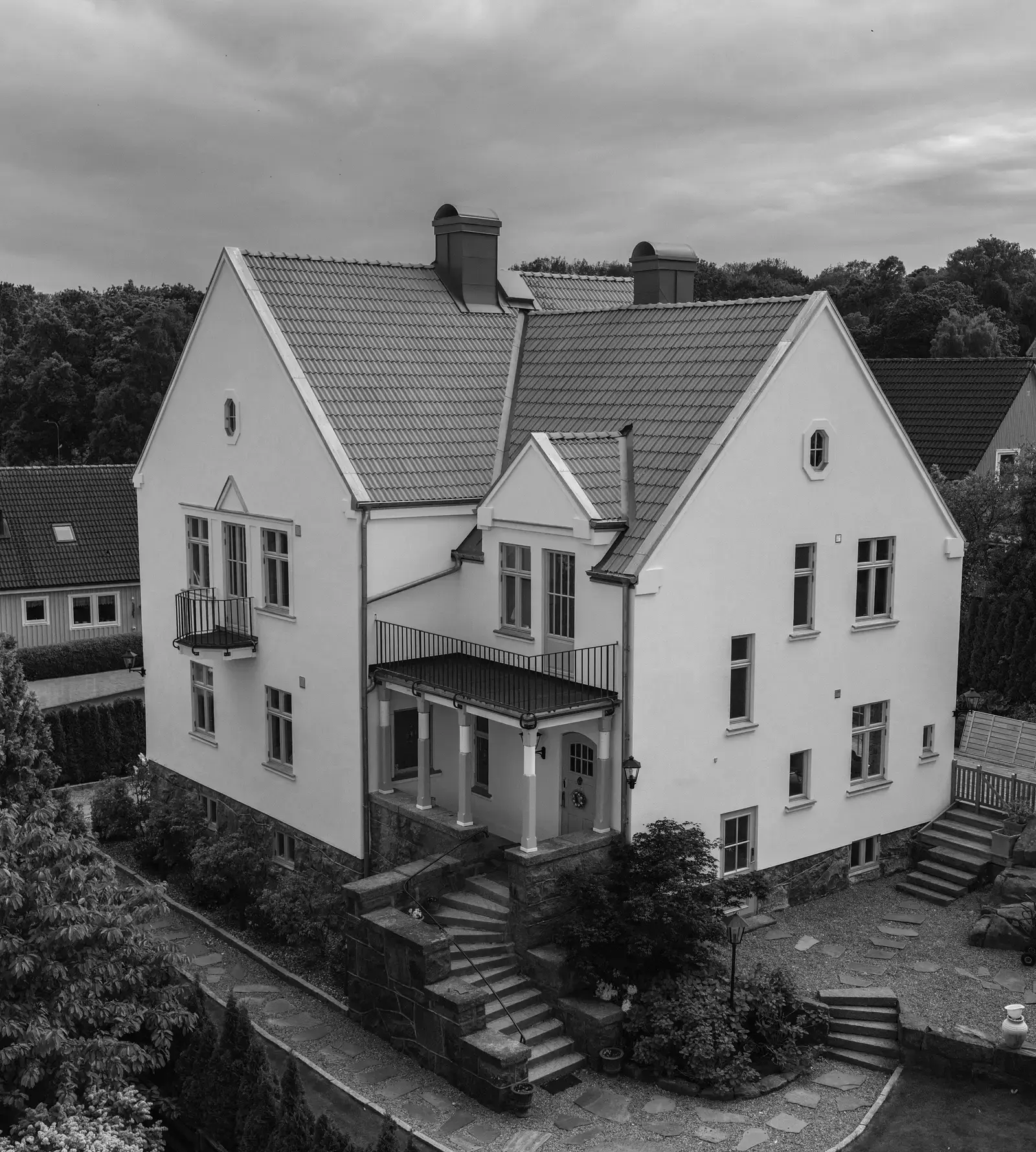 Stor vit villa med tegeltак och veranda, fotograferad från luften.